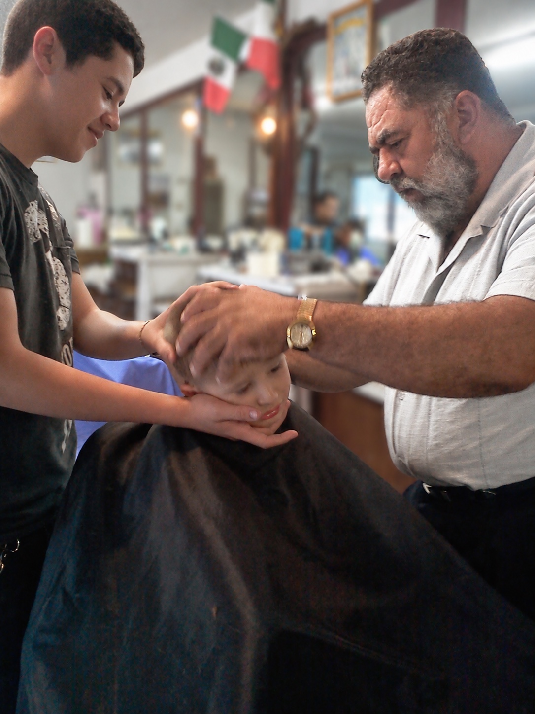 Ricardo and his father cutting a young client’s hair inside the family barbershop